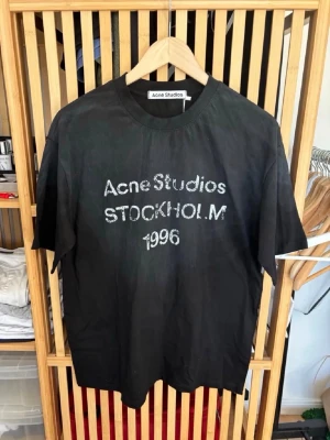 Svart Acne Studios t-shirt - Cool svart t-shirt från Acne Studios med tryck 'Acne Studios STOCKHOLM 1996' på bröstet. Klassisk rund hals och korta ärmar. Perfekt för dig som gillar stilrena plagg med en twist. Storlek M och i oanvänt skick.