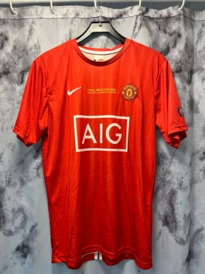 Manchester United Ronaldo tröja 2008 - Röd Manchester United matchtröja från Nike med tryck 'Ronaldo 7' på ryggen och AIG som sponsor på bröstet. Framtill står det 'Final Moscow 2008', och klubbmärket sitter på vänster bröst. Korta ärmar och rund hals, perfekt för fotbollsfans.