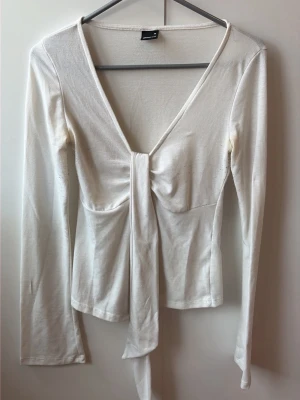 Vit omlottopp med knyt framtill - Trendig vit omlottopp med lång ärm och djup v-ringning. Toppen har ett snyggt knyt framtill som ger en feminin siluett. Perfekt att styla med jeans eller kjol för en cool look. Det är fläckar i armhålorna men inget märkbart! 