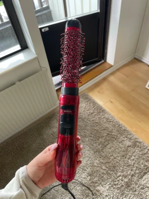 Röd varmluftsborste med roterande funktion - Säljer en röd varmluftsborste med roterande borsthuvud och svart handtag. Perfekt för att styla håret och skapa volym. Borsten har ett smidigt grepp och sladd för enkel användning. Passar dig som vill fixa frisyren snabbt och enkelt.