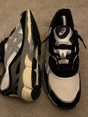 Svarta och vita Asics sneakers - Snygga sneakers från Asics i svart, vitt och grått. Ovandelen är i mesh och syntetmaterial med tydliga Asics-loggor på sidan och tungan. Skorna har tjock, dämpad sula och svarta snören. Perfekta för en sportig och trendig look.Priset går att diskutera vid snabb affär, finn de frågor så är de bara o skriv 😊