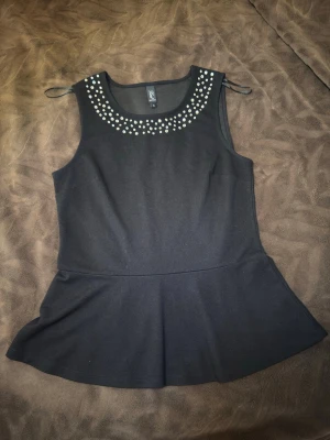 Svart kort klänning med nitar - Svart kort klänning från H&M med ärmlös design och rund halsringning dekorerad med silvriga nitar. Klänningen har en lätt utställd kjol och är tillverkad i ett mjukt material som ger en bekväm passform. Perfekt för dig som gillar stilrena detaljer.