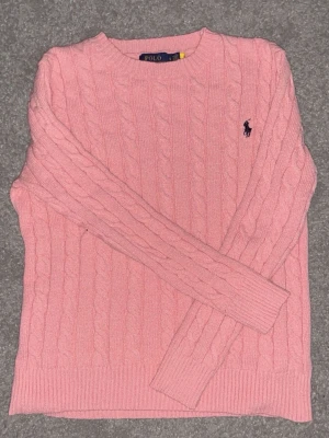 Rosa kabelstickad tröja Polo Ralph Lauren - Supersnygg rosa kabelstickad tröja från Polo Ralph Lauren. Klassisk modell med rund halsringning, ribbade muddar och det ikoniska lilla logobroderiet på bröstet. Perfekt till jeans eller kjol för en chill och stilren look.