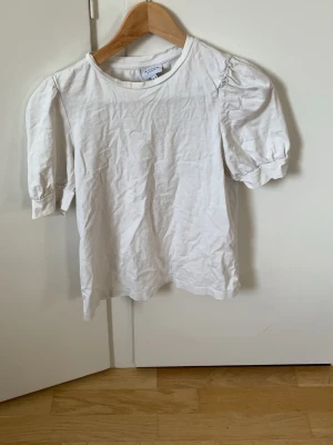 Vit puffärmad t-shirt från Vero Moda - Säljer en vit t-shirt från Vero Moda med puffärmar och rund halsringning. T-shirten är gjord i mjuk bomull och har en enkel, stilren design som passar till det mesta. Perfekt för dig som gillar en basic men ändå trendig look.