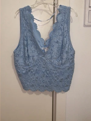 Blå spetslinne med djup urringning - Snyggt blått linne i spets med djup v-ringning och blommigt mönster. Toppen är ärmlös och har en feminin, figurnära passform. Perfekt att styla med jeans eller kjol för en trendig look. köpt i New yorker