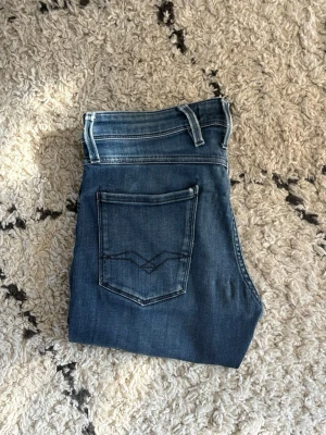 REPLAY ANBASS - Snygga blå jeans med raka ben och klassisk femficksdesign. Jeansen har en cool tvättad look och kontrastsömmar på fickorna. Passar perfekt till en avslappnad stil och har bälteshällor i midjan.
