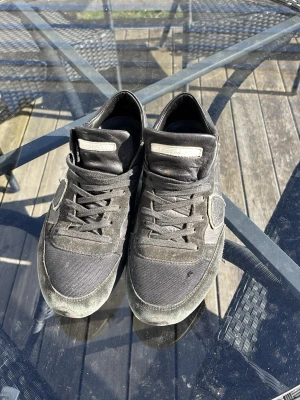 Svarta sneakers från Philippe Model - Säljer ett par svarta sneakers från Philippe Model med snygga detaljer i mocka och textil. Skorna har klassisk låg profil, svarta skosnören och en vit logotyp på plösen. Perfekta för dig som gillar stilrena och tidlösa sneakers.