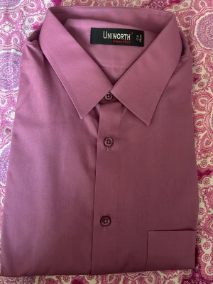 Ljuslila skjorta ~ XL - Säljer en stilren ljuslila skjorta från Uniworth med klassisk krage och knappar framtill. Skjortan är tillverkad i ett mjukt material och passar perfekt till dig som vill ha en enkel men snygg look. Storlek 44 (17.5 tum). Skjortan är helt ny men saknar prislapp!