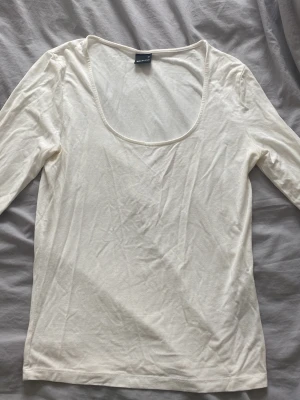 Vit långärmad topp med djup rund hals - Säljer en enkel och stilren vit långärmad topp med djup rundad halsringning. Materialet är mjukt och stretchigt, perfekt för layering eller att bära som den är. Ärmarna har en liten slitsdetalj som ger en cool touch. Passar dig som gillar basic och clean look.