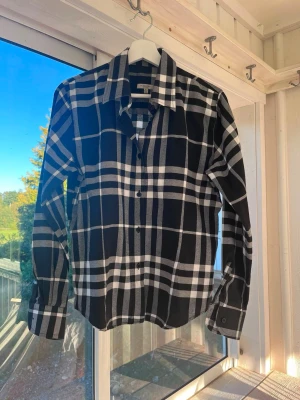 Svartvit rutig skjorta Burberry  - Säljer en svartvit rutig skjorta från Burberry i storlek XL. Skjortan har klassisk krage, knäppning framtill och långa ärmar med manschett. Tillverkad i mjuk bomull och har en tidlös design som sticker ut. Den är dam skulle jag tro men den känns som S, inte XL!!