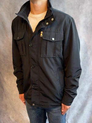 J-Lindeberg Bailey Fieldjacket- Stl L - Riktigt snygg Vår/Höst Bailey Fieldjacket från J-Lindeberg i färgen svart! | Mycket bra skick: 9/10, inga defekter | Stl: L,  modellen är 178cm och väger 78kg, passar bättre mellan 182--195cm 🙌  | Hör av dig vid frågor // Galgen 🫡