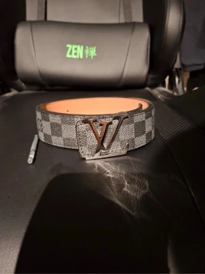 Rutigt svart och grått bälte - Snyggt bälte med klassiskt rutigt mönster i svart och grått samt ett stor metallspänne. Bältet har en exklusiv känsla och passar perfekt till jeans eller kostymbyxor. Insidan är ljusbrun och materialet känns robust.