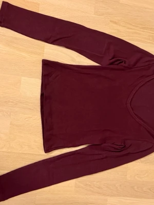 Vinröd långärmad topp - En enkel och stilren vinröd topp med lång ärm och v-ringad halsringning. Perfekt att matcha med jeans eller kjol för en clean look. Materialet känns mjukt och stretchigt.