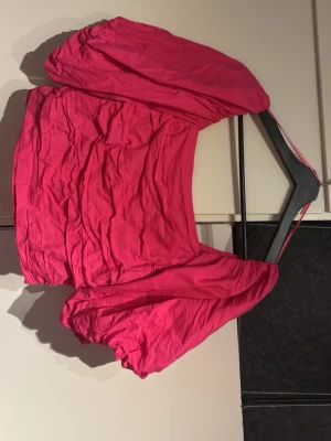 Rosa croppad blus med puffärmar - Trendig rosa blus med croppad passform och puffiga korta ärmar. Toppen har en fyrkantig urringning och smockad detalj framtill som ger en snygg siluett. Perfekt för dig som vill sticka ut med färg och volym.