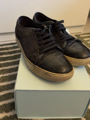 Svarta Lanvin  - Snygga svarta sneakers från Lanvin i äkta läder med klassisk låg profil och svarta skosnören. Skorna har en beige sula med Lanvin-logga undertill och passar perfekt till en stilren och avslappnad look.