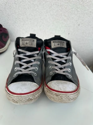 Converse sneakers - Klassiska Converse All Star sneakers i grått med vita tår och sulor, röda detaljer och vita skosnören. Skorna har den ikoniska All Star-loggan på sidan och är tillverkade i canvas med gummisula och den är lite smutsig i bilden men kan tvättas och bli till en lagom sneaker. Perfekta för en avslappnad streetstyle-look. Bra pris! 