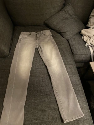 Grå raka jeans med tvättad look - Säljer ett par grå jeans med rak passform och tvättad effekt. Klassisk femficksmodell med knapp och dragkedja framtill. Jeansen har en stilren look som passar till det mesta och är tillverkade i ett mjukt denimtyg. Och ingen har någonsin tagit på sig de