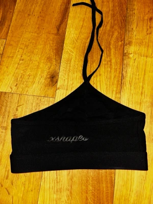 Svart halterneck bh - Snygg svart bh i halterneck-modell med knytband i nacken. Bh:n har ett brett band under bysten.Tillverkad i mjukt stretchigt material för bekväm passform.