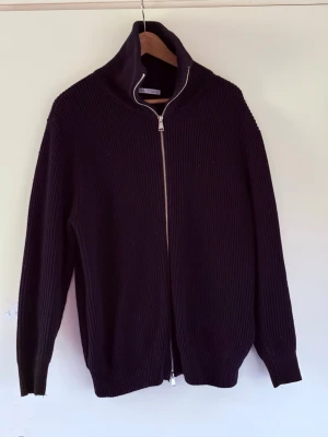 Marinblå stickad ziptröja från Zara - Marinblå stickad tröja från Zara med dragkedja hela vägen och hög krage. Tröjan har ribbad struktur och långa ärmar, perfekt för lager-på-lager. Enkel och stilren design som passar till det mesta.