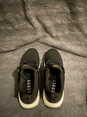 Ultra boost svart vita - Snygga svarta sneakers med BOOST-sula och stickad ovandel. Skorna har svarta skosnören och en vit, dämpad sula som ger skön komfort. Perfekta för dig som gillar sportig och modern stil. Ovandelen är i mesh-liknande material för bra andningsförmåga.