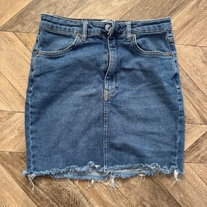 Blå jeanskjol från Pull&Bear - Säljer en blå jeanskjol från Pull&Bear i klassisk modell med fem fickor och rå fransig kant nedtill. Kjolen har normal passform och stängs med knapp och dragkedja framtill. Perfekt till sneakers eller boots!