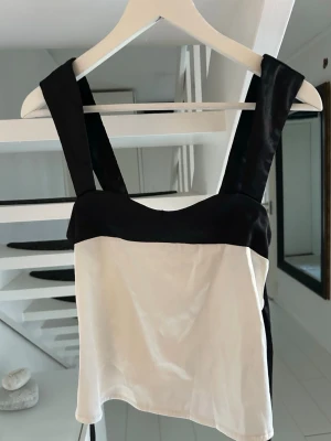 Svartvit linnetopp med breda band - Snygg svartvit linnetopp med breda axelband och kontrastfärgade detaljer. Toppen har en rak passform och knytband i ryggen för extra stilpoäng. Perfekt att matcha med jeans eller kjol för en trendig look.