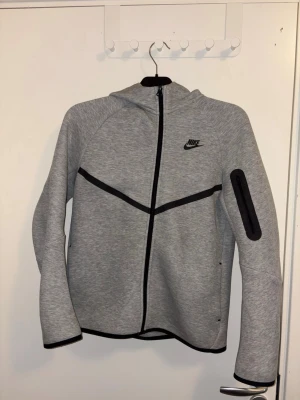 Grå Nike Tech Fleece - Säljer en grå Nike tech fleece zip up tröja för den är för liten. Den är i väldigt bra skicka då den är sparsamt använd. ANVÄND GÄRNA INSTABOX!