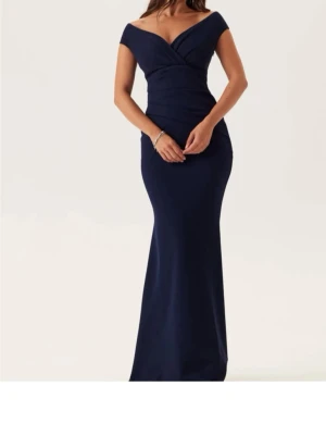 Marinblå långklänning offshoulder - Elegant marinblå långklänning med offshoulder-design och v-ringad omlottdetalj framtill. Klänningen har en figurnära passform och är perfekt för speciella tillfällen. Materialet ser ut att vara mjukt och följsamt.