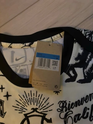 Nike t-shirt med svartvitt tryck - Cool t-shirt från Nike med svartvitt grafiskt tryck och kontrasterande svarta detaljer vid kragen. T-shirten har korta ärmar och är tillverkad i ett lätt och bekvämt material, perfekt för en avslappnad streetstil.