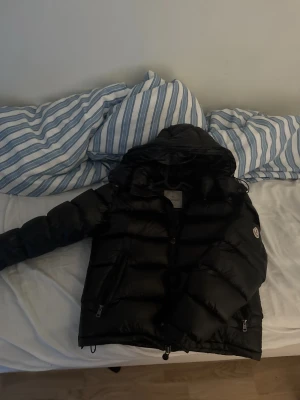Moncler svart men  - Säljer en svart dunjacka från Moncler med huva och två dragkedjefickor framtill. Jackan har en puffig design och Moncler-logga på ärmen. Perfekt för kalla vinterdagar och riktigt snygg till streetwear-stilen.