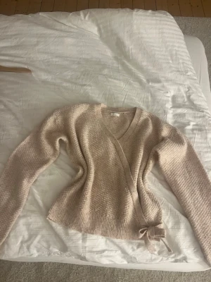 Beige omlottkofta från NEXT - Mysig beige stickad omlottkofta från NEXT med knytband i midjan och v-ringad hals. Koftan har ett diskret rutmönster i stickningen och ribbade muddar vid ärmslut och nederkant. Perfekt för lager på lager och en avslappnad look. Säljer för den passar inte mig längre tyvärr annars älskar jag den, vet tyvärr inte vilken storlek men den är nog xs💞
