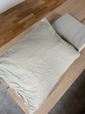 Beige bäddset i bäckebölja x4 - Säljer ett stilrent bäddset i beige med quiltad struktur. Setet innehåller ett påslakan och ett örngott i mjuk textil, perfekt för en enkel och modern känsla i sovrummet.