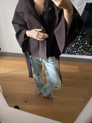 Mörkbrun cape-kappa med knytband - Säljer en mörkbrun cape-kappa med bred krage och knytband i midjan som ger en fin figur! Säljer pga har en likadan i annan färg. 