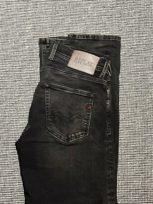 Svarta Replay Hyperflex jeans - Snygga svarta jeans från Replay med Hyperflex-teknologi som ger extra stretch och komfort. Klassisk femficksmodell med Replay-logga på bakfickan och metallmärke i midjan. Perfekta för en trendig och avslappnad stil.