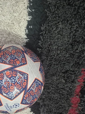 Champions League fotboll med mönster - Säljer en Champions League fotboll med vita, blå och orange detaljer. Bollen har ett stjärnmönster och tryck med Champions League-loggan. Tillverkad i slitstarkt syntetmaterial och passar perfekt för både spel och träning.