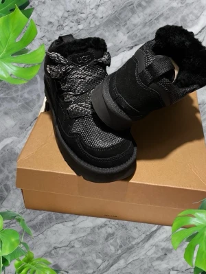 Svarta Ugg Lowmel - Snygga svarta Ugg Lowmel med grov snörning och fluffigt foder. Ovandelen är i en mix av textil och mocka, med robust platt sula och rund tå. Perfekta för kyliga dagar och ger en cool look till din outfit. Endast provade 