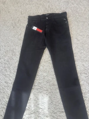 Svarta slim jeans från Replay - Snygga svarta slim fit jeans från Replay med klassisk femficksdesign och knappgylf. Jeansen har en stilren look och är tillverkade i ett mjukt och stretchigt material som sitter skönt. Perfekta för dig som gillar en modern och clean stil. Nya replay jeans me prislappar o allt kvar 