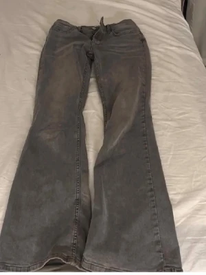 Gråa utsvängda jeans - Säljer ett par gråa jeans med utsvängda ben och klassisk femficksmodell. Jeansen har hög midja och dragkedja med knapp framtill. Perfekta för dig som gillar retrostil och vill ha ett par bekväma och snygga jeans i garderoben.