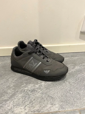Grå EA7 Emporio Armani sneakers - Snygga grå sneakers från EA7 Emporio Armani med mesh och syntetpaneler. Skorna har svarta snören, logga på sidan och svart sula. Perfekta för dig som gillar stilrena och sportiga skor med en modern touch.