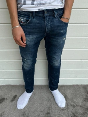Diesel jeans marinblå med slitningar - Hej, otroligt snygga diesel jeans med slitningar i nyskick säljes. Modellen på bilden är 183cm och väger 68kg. Passformen är slim och heter Thommer. Storleken är W31/L32. 95% bomull, 3% polyester och 2% elastan. Hör av dig vid intresse! Mvh 