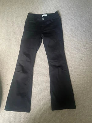 Svarta bootcut jeans - Snygga svarta bootcut jeans med klassisk femficksdesign och utsvängda ben. Jeansen har knapp- och dragkedjestängning samt är tillverkade i ett mjukt denimtyg som sitter skönt. Perfekta för dig som gillar en retroinspirerad look.
