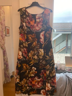 Blommig långklänning från Voglia - Snygg klänning från Voglia med stort blommigt mönster i färger som vinröd, beige, grön, orange och svart. Klänningen är ärmlös och har en rund halsringning, den har också dragkedja på baksidan. Perfekt för dig som vill sticka ut med en färgstark look.                                                                                     Är öppen för att förhandla priset🌸