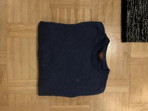 Marinblå merinoulltröja från Morris - Snygg marinblå tröja från Morris i 100% merinoull. Klassisk rund hals och diskret logga broderad på bröstet. Långärmad med ribbade muddar vid ärmslut och nederkant. Perfekt för dig som gillar stilrena och bekväma plagg. För frågor eller funderingar skriv gärna! Priset är ej hugget i sten!😁
