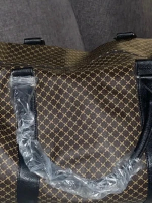 Brun weekendbag med mönster - Snygg brun weekendbag med guldfärgat rutmönster och svarta detaljer. Väskan har två svarta handtag och är tillverkad i ett tåligt material som liknar konstläder. Perfekt för resor när du vill ha stil och funktion i ett.