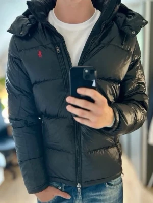 Svart pufferjacka från Polo Ralph Lauren - Mycket fint skick, endast en liten defekt(be om bild vid intresse). Nypris ca 6000kr. Storlek S passar mellan 175-190 ungefär beroende på hur man vill ha den. Modellen är 185 cm. Skriv för mer information!