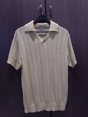 Beige/ grön  stickad topp från Zara - Säljer en beige stickad topp från Zara med v-ringning och krage. Toppen har korta ärmar och ett diskret ribbat mönster som ger en snygg struktur. Perfekt till jeans eller kjol för en avslappnad men stilsäker look.