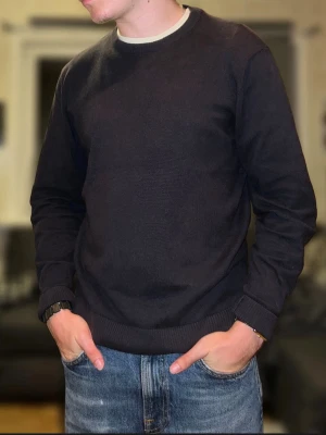 Mörkblå stickad tröja från Zara - En stilren mörkblå stickad tröja från Zara med Storlek S men passar mer som M. Tröjan har rund halsringning och ribbade muddar vid ärmslut och nederkant. Perfekt för att hålla värmen under kyligare dagar och passar till jeans eller chinos.