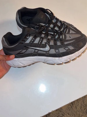 Nike grå och svarta sneakers - Snygga sneakers från Nike i grått och svart med vit sula. Skorna har ett sportigt rutmönster i mesh och syntet, samt den klassiska Nike-loggan på sidan. Lågt skaft och snörning framtill för en clean look.