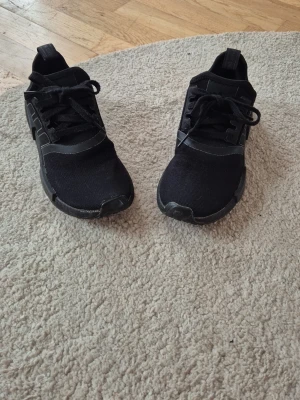 Svarta sneakers i textil och syntet - Snygga svarta sneakers från Adidas med ovandel i mesh och syntetdetaljer. Klassisk låg modell med snörning och diskret logga på plösen. Perfekta för en sportig och stilren look. Använda några få gånger.  Hund finns i hemmet. 