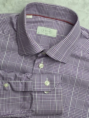 Eton Slim skjorta rutig lila/vit storlek S / 38 / 15 - Rutig skjorta från Eton i Slim-passform. Stilren lila och vit design med småskaligt rutmönster. Klassisk modell som fungerar både till vardag och mer uppklätt. Tillverkad i 100% bomull.  Storlek S / 38 / 15 Slim Fit  Mycket fint skick.  Mått  Bröstbredd: ca 50 cm Plagglängd: ca 74 cm Axelbredd: ca 44 cm Ärmlängd: ca 67 cm  Material 100% bomull  Varan är begagnad och säljs i befintligt skick, se bilder för detaljer.